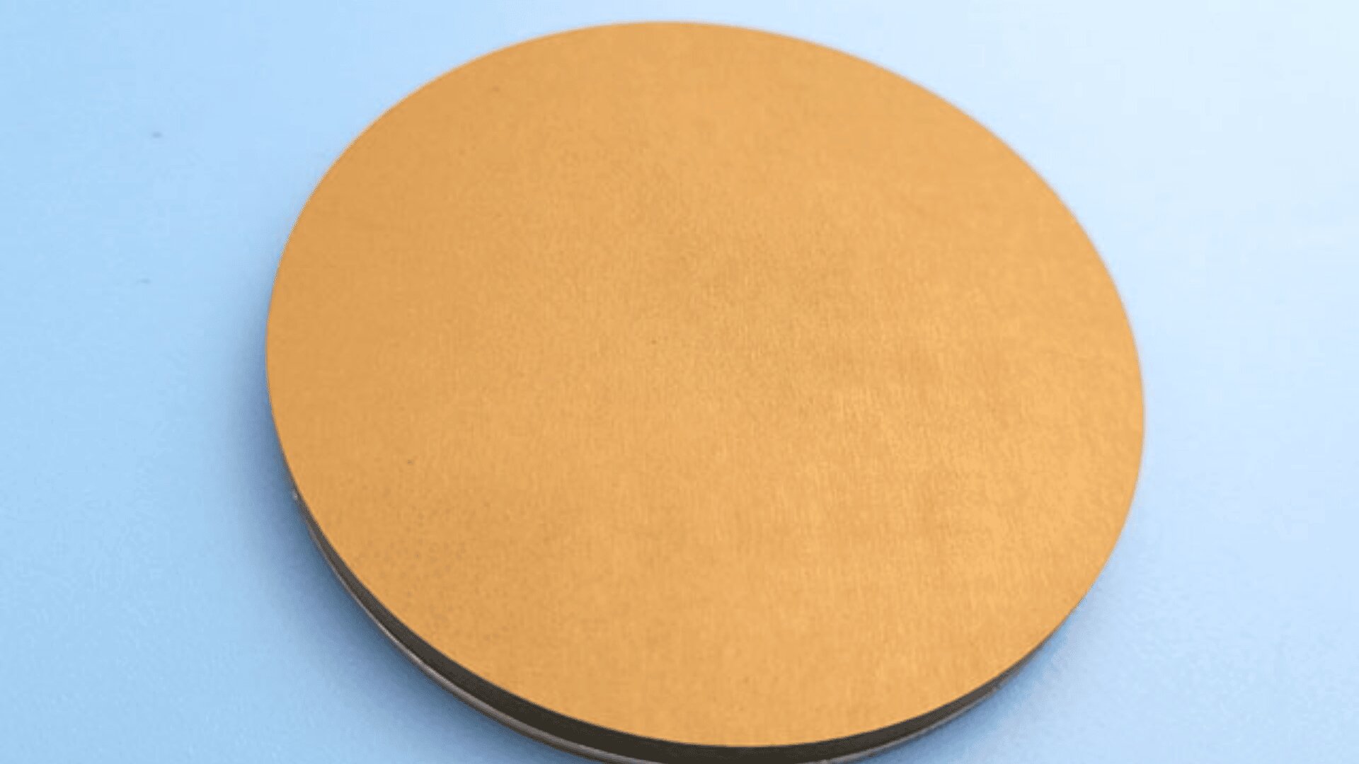 A round, flat, gold-colored disc rests on a light blue surface.