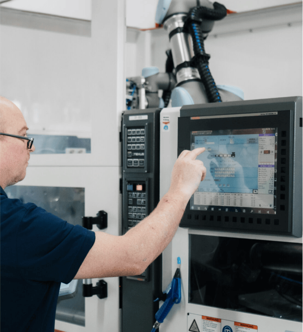 Eine Person in einem marineblauen Hemd bedient ein Touchscreen-Bedienfeld an einer Industriemaschine in einer modernen Produktionsumgebung.