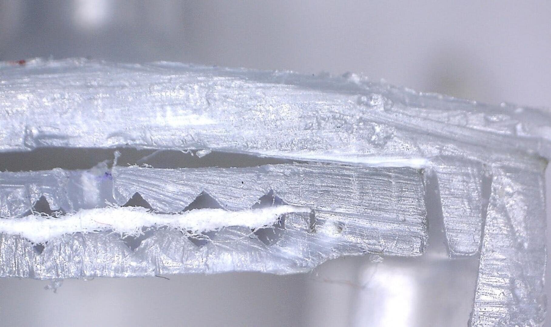 Close-up of a metal or plastic object that has a rough, cut edge with visible grooves and serrations, possibly part of a mechanism or tool, photographed under magnification.