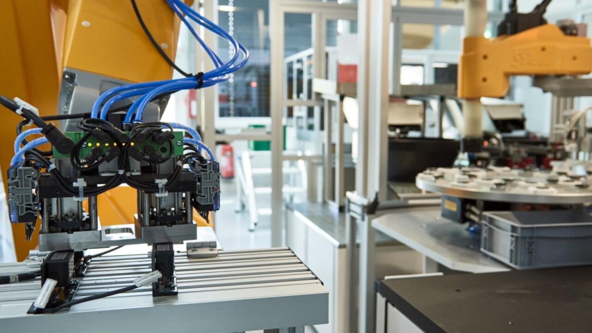 Close-up of robotic arms and automated machinery in a modern factory setting, featuring wires, sensors, and metal grippers, illustrating advanced manufacturing and industrial automation.