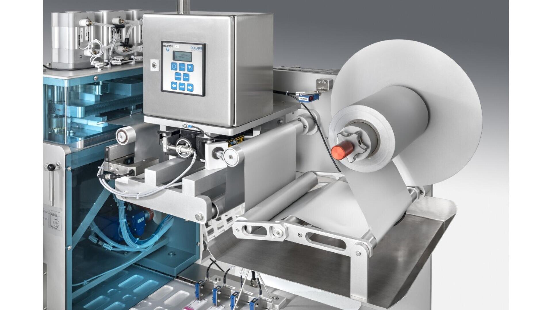 A close-up view of industrial packaging machinery with a roll of white film, a control panel with buttons and display, and various metallic components and mechanisms.