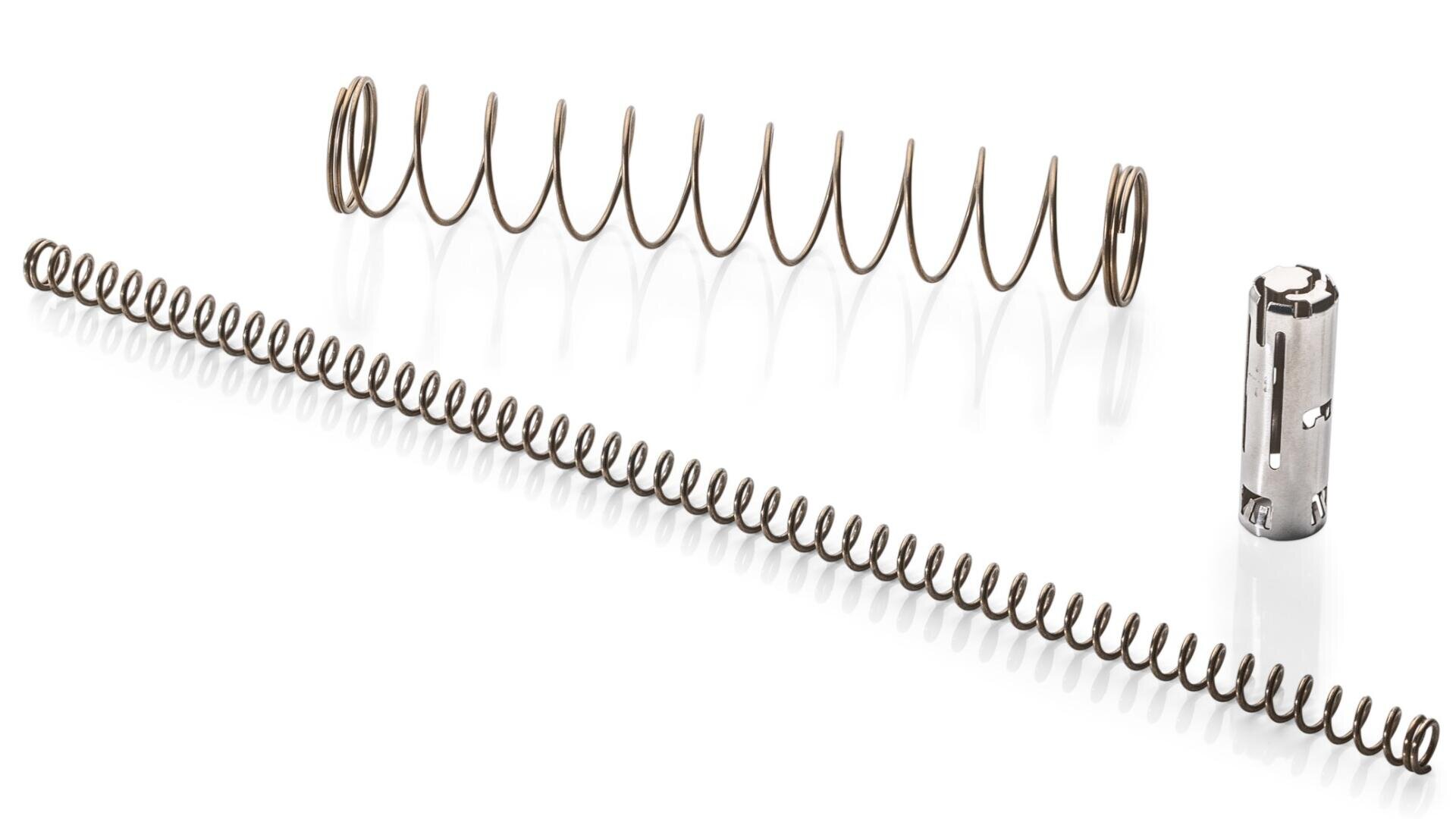 Es werden drei Metallobjekte gezeigt: zwei Spiralfedern, eine fest und eine locker gewickelt, und ein kleines zylindrisches Metallteil mit Ausschnitten, alle auf weißem Hintergrund.