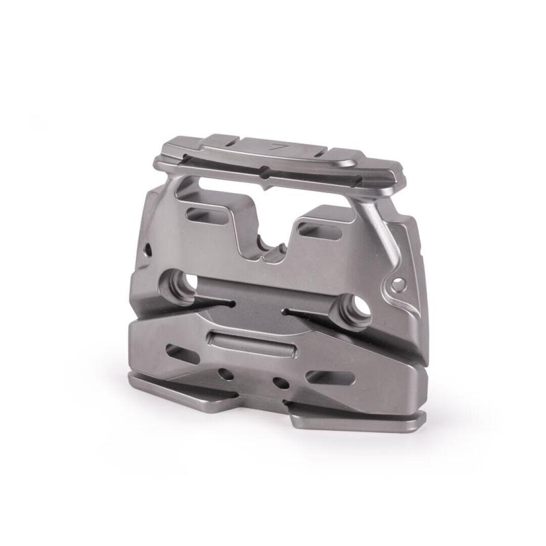 A metallic, machined component with various cutouts, holes, and grooves, standing upright on a white background. The part appears to be precisely engineered, possibly for industrial or mechanical use.