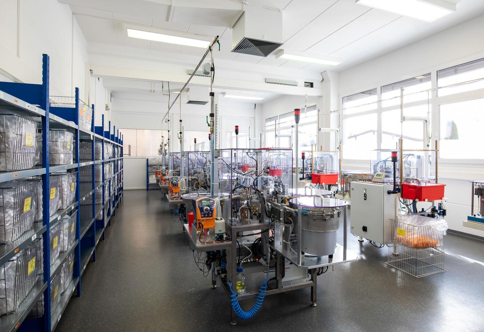 Ein Laborraum mit großen Fenstern, links Regalen mit durchsichtigen Käfigen und rechts Reihen automatisierter Geräte und Maschinen für die Laborforschung.