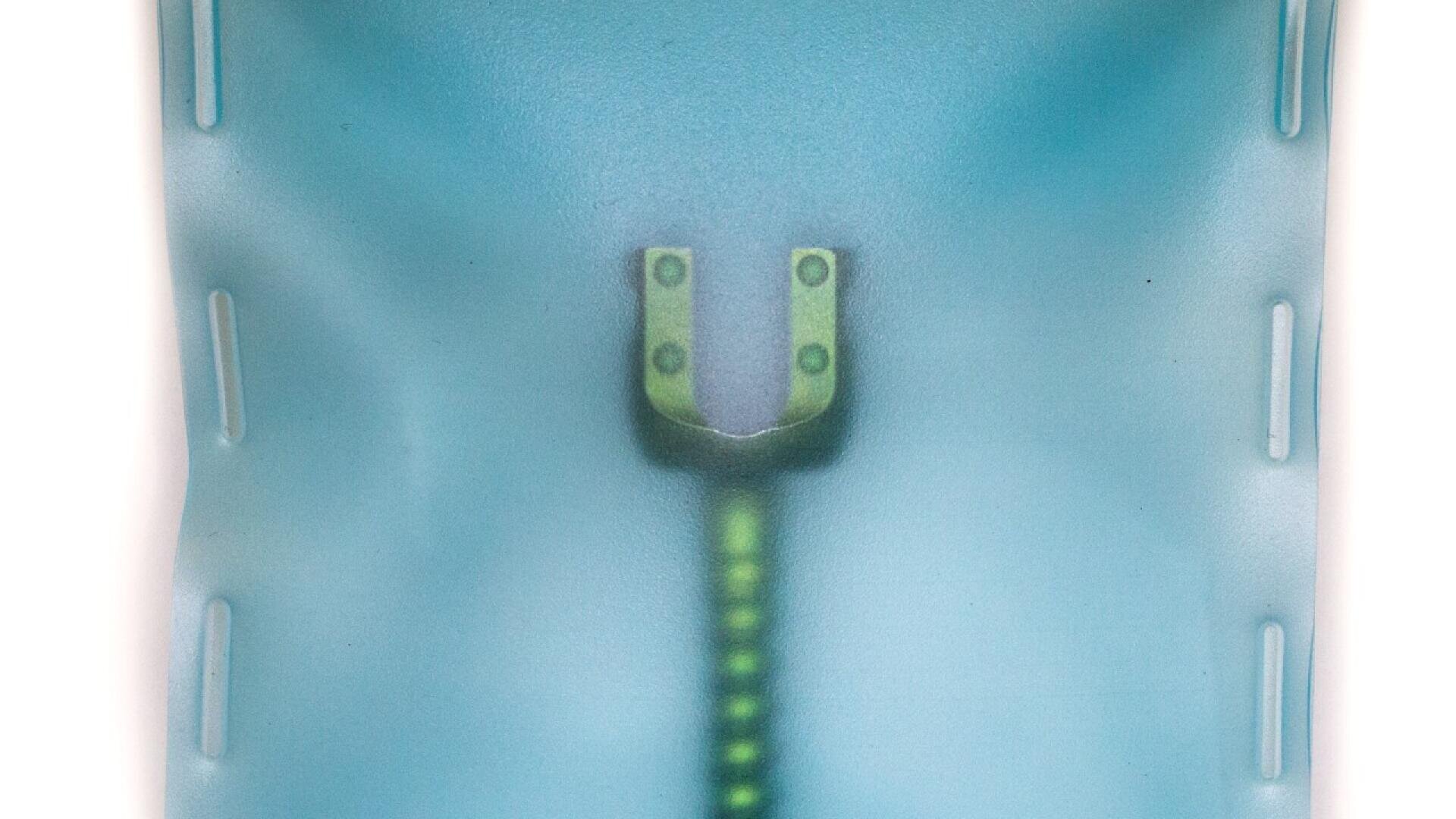 Nahaufnahme einer blauen Oberfläche mit einem teilweise geöffneten Reißverschluss, der in der Mitte eine grüne Reißverschlussspur und einen metallischen Reißverschlusszug erkennen lässt. Das blaue Material erscheint leicht durchscheinend und ist mit vertikalen Nähten gepolstert.