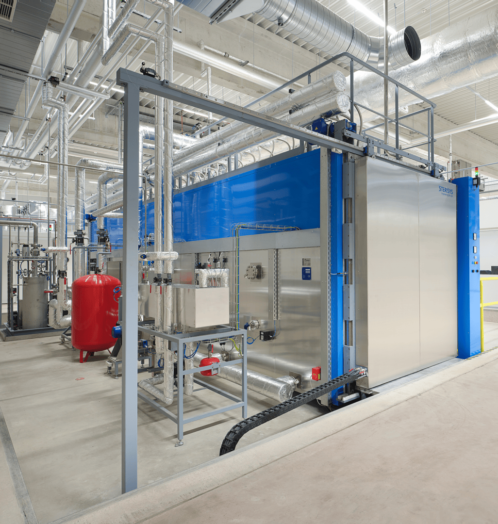 Eine moderne Industrieanlage mit großen Maschinen aus Edelstahl und Blau, sichtbaren Rohren, Kanälen und Bedienfeldern, die auf einem sauberen Betonboden unter heller Deckenbeleuchtung stehen.