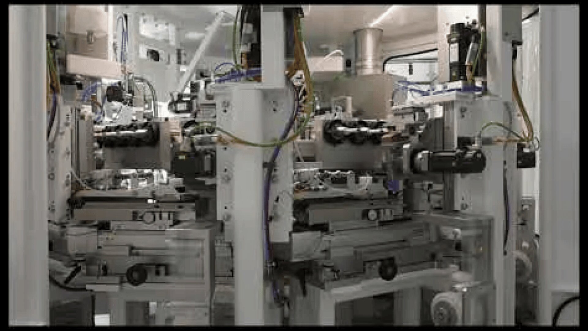 Nahaufnahme einer komplexen Industrieanlage mit Metallteilen, Kabeln und Sensoren in einer sauberen, modernen Produktionsstätte. Die Geräte scheinen automatisiert zu sein und werden für die Präzisionsfertigung oder Montage verwendet.