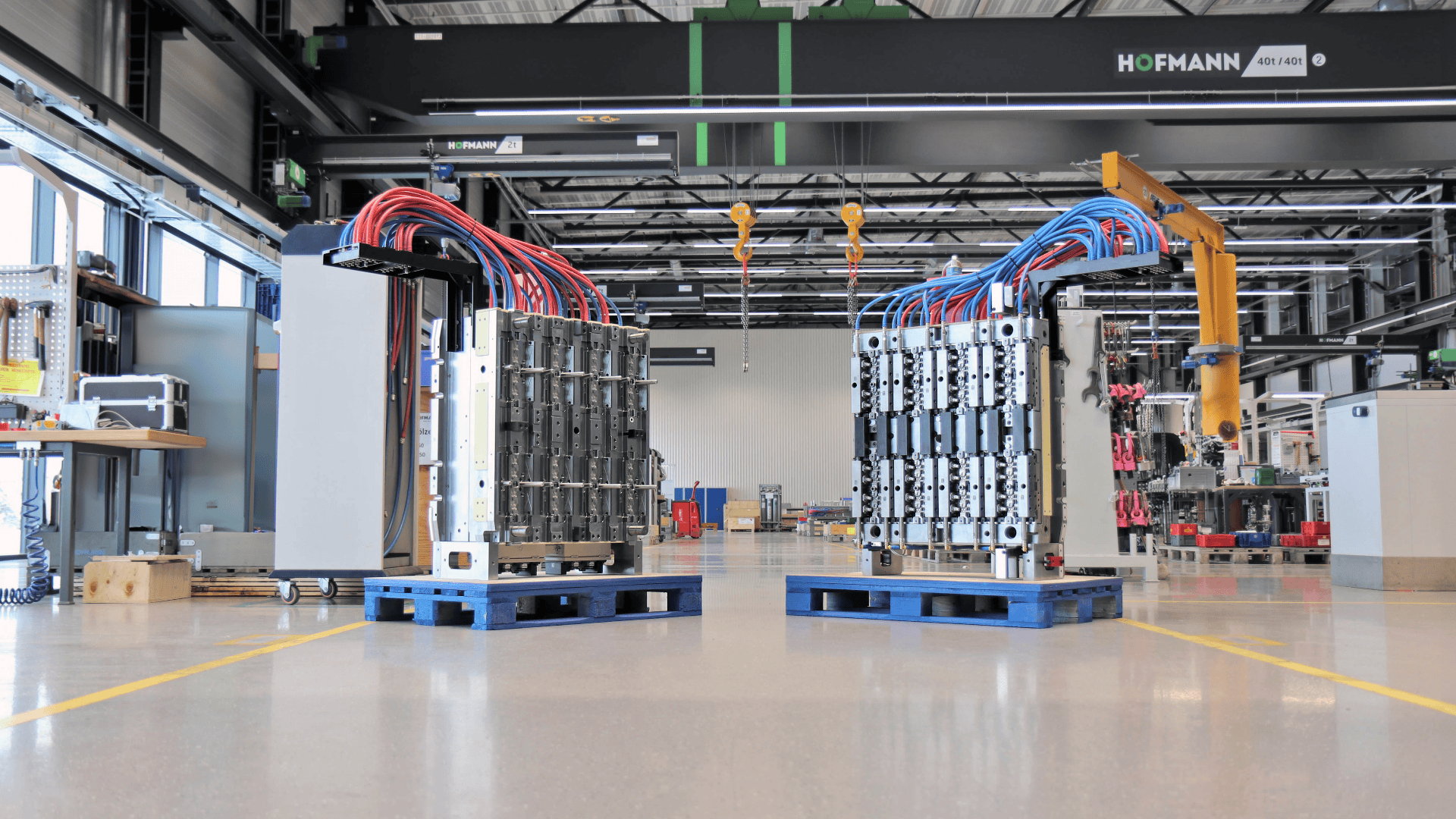 Zwei große elektrische Industriemodule mit mehreren Drähten, meist rot und blau, sind auf blauen Paletten in einer geräumigen, modernen Fabrik mit Maschinen und Geräten im Hintergrund montiert.