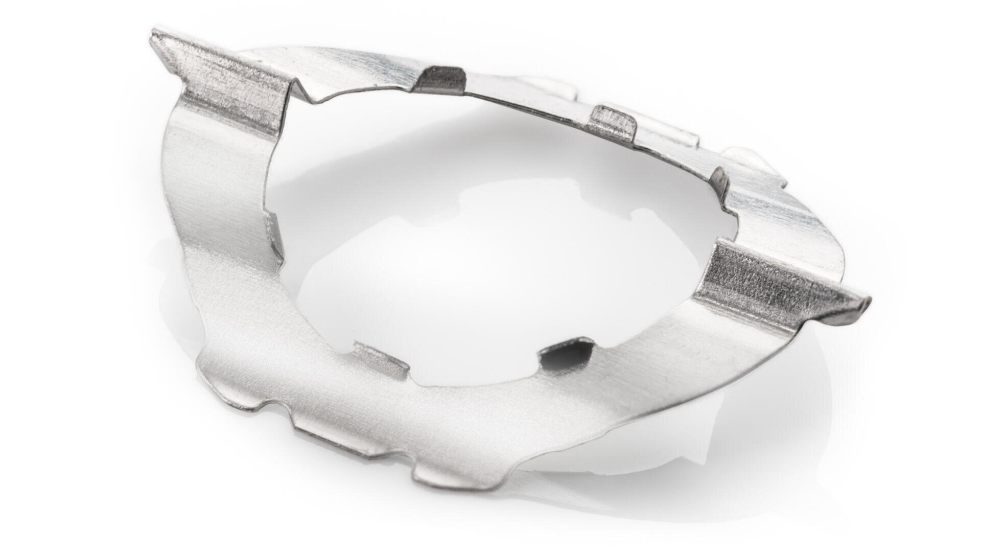 Nahaufnahme eines kleinen, dünnen, metallischen Bauteils mit gebogenen Rändern und ausgeschnittenen Bereichen auf weißem Hintergrund.
