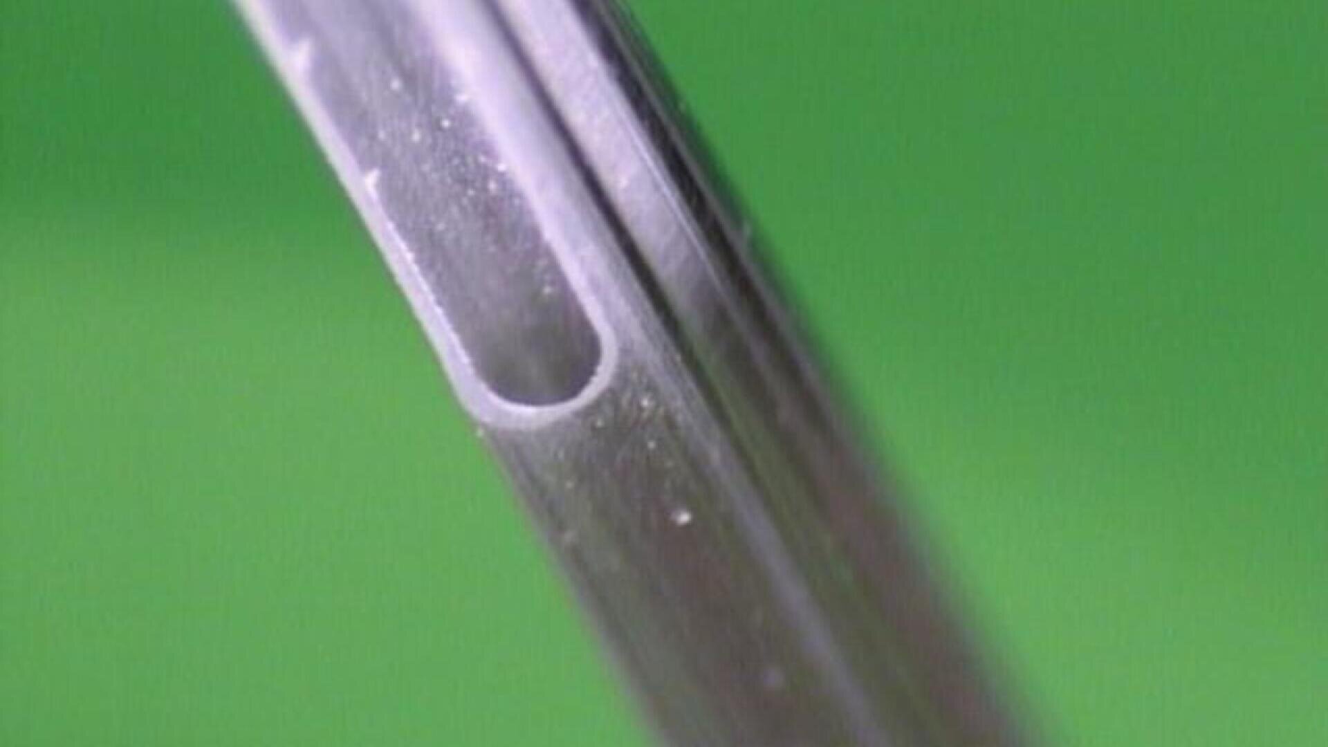 Close-up of the bevelled tip of a hypodermic needle against a green background.
