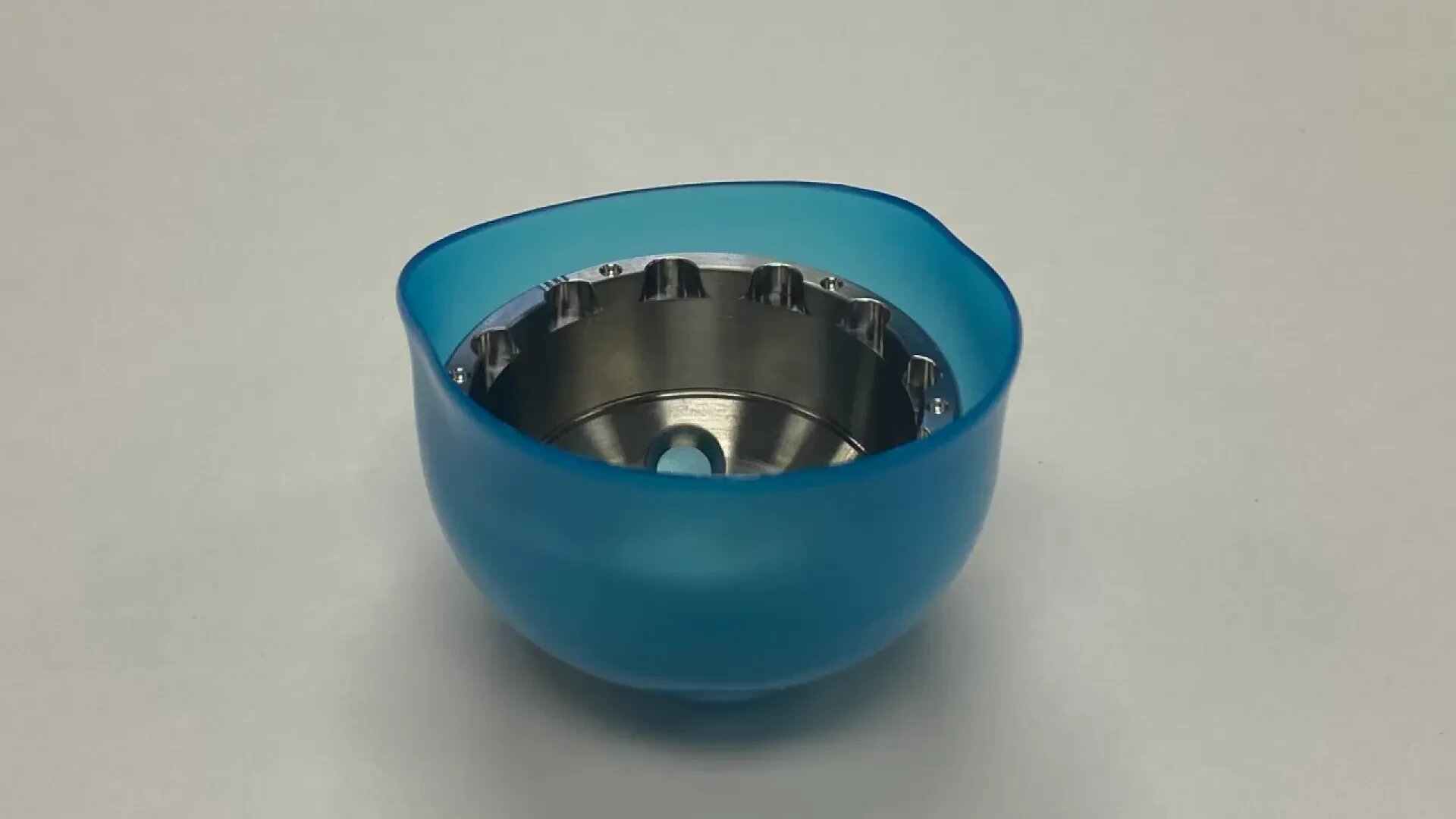A small, round, blue plastic container with a metal interior featuring evenly spaced notches along the rim, placed on a plain white surface.