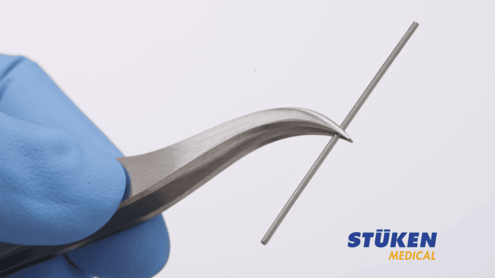 A gloved hand holds a curved metal tool gripping a thin metal rod, with the STÜKEN Medical logo in the lower right corner.