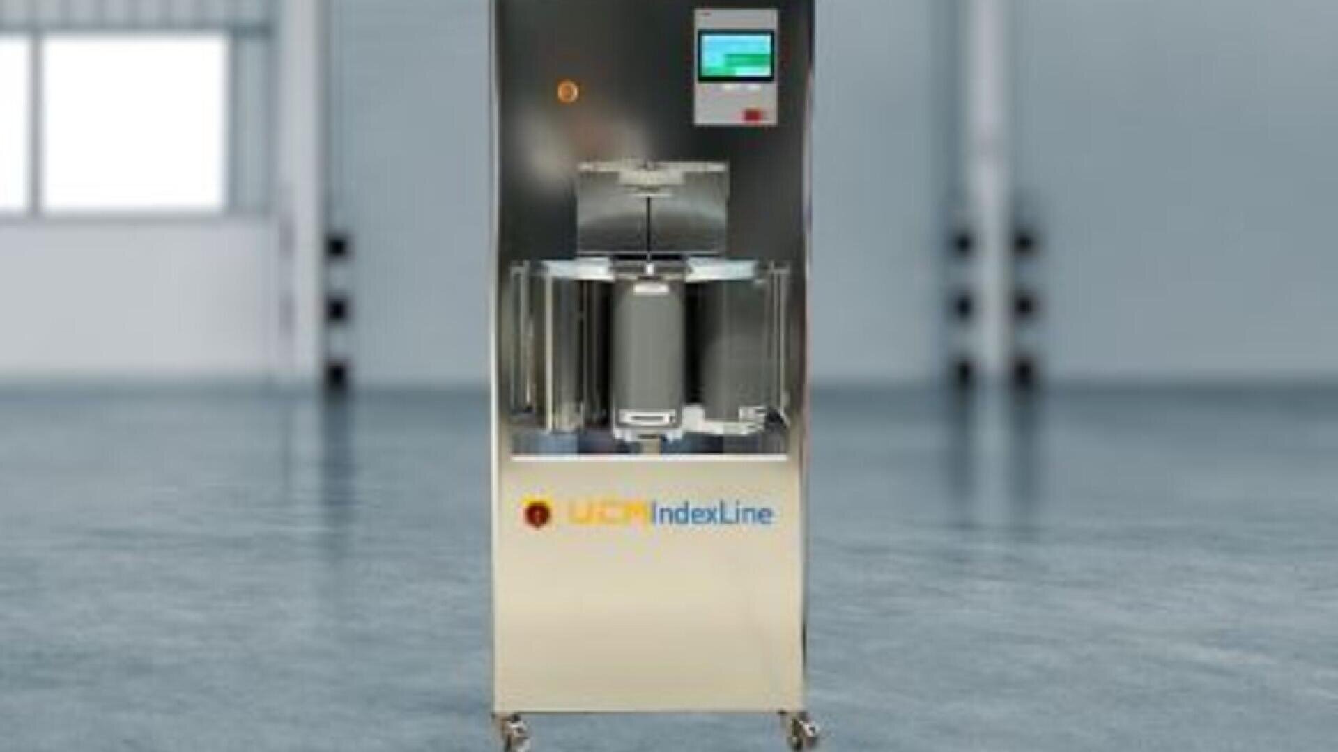 A stainless steel industrial machine on wheels with a digital screen and control panel, labeled UCR IndexLine, standing in a spacious, modern factory setting.