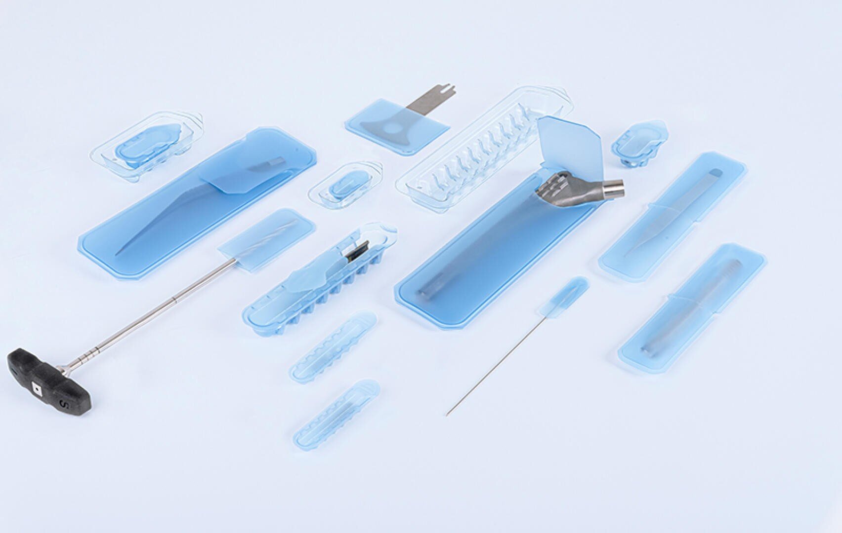 Ein Satz sterilisierter medizinischer Instrumente und Werkzeuge in einer blauen Kunststoffverpackung, angeordnet auf einem weißen Hintergrund. Das Set enthält Nadeln, einen Griff, ein gebogenes Metallstück und verschiedene Kleinteile.