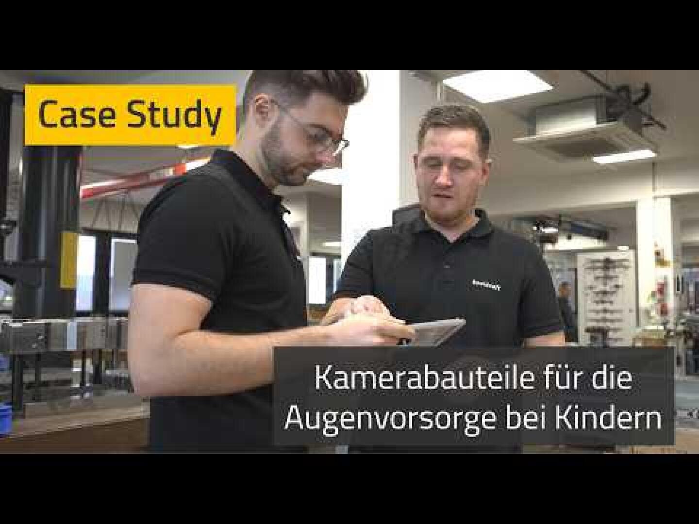 Zwei Männer in schwarzen Hemden stehen in einem Haus und schauen gemeinsam auf ein Tablet. In einem Text-Overlay steht: Fallstudie. Kamerabauteile für die Augenvorsorge bei Kindern", was so viel bedeutet wie "Kamerabauteile für die Augenvorsorge bei Kindern".