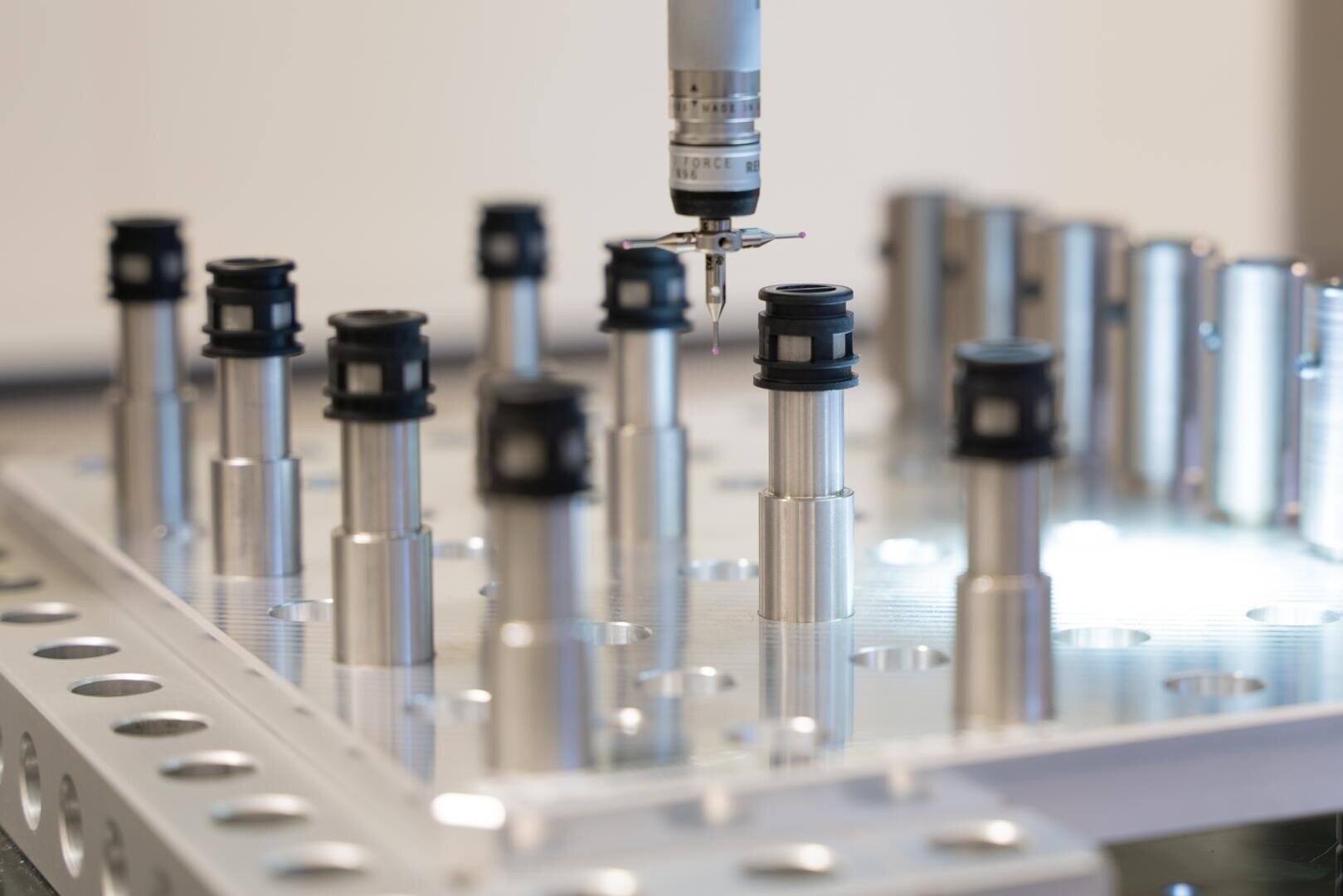 A precision measuring probe inspects metal cylindrical components mounted on a fixture in a laboratory or industrial setting, highlighting advanced manufacturing and quality control processes.