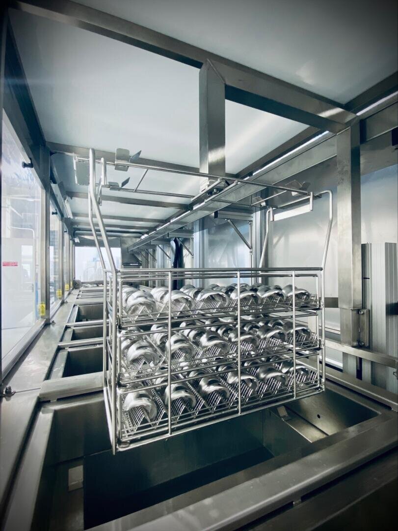 Ein Metallgestell mit ordentlich angeordneten Edelstahllöffeln wird in einer sauberen, modernen Anlage in eine industrielle Geschirrspül- oder Sterilisationsmaschine gehängt.