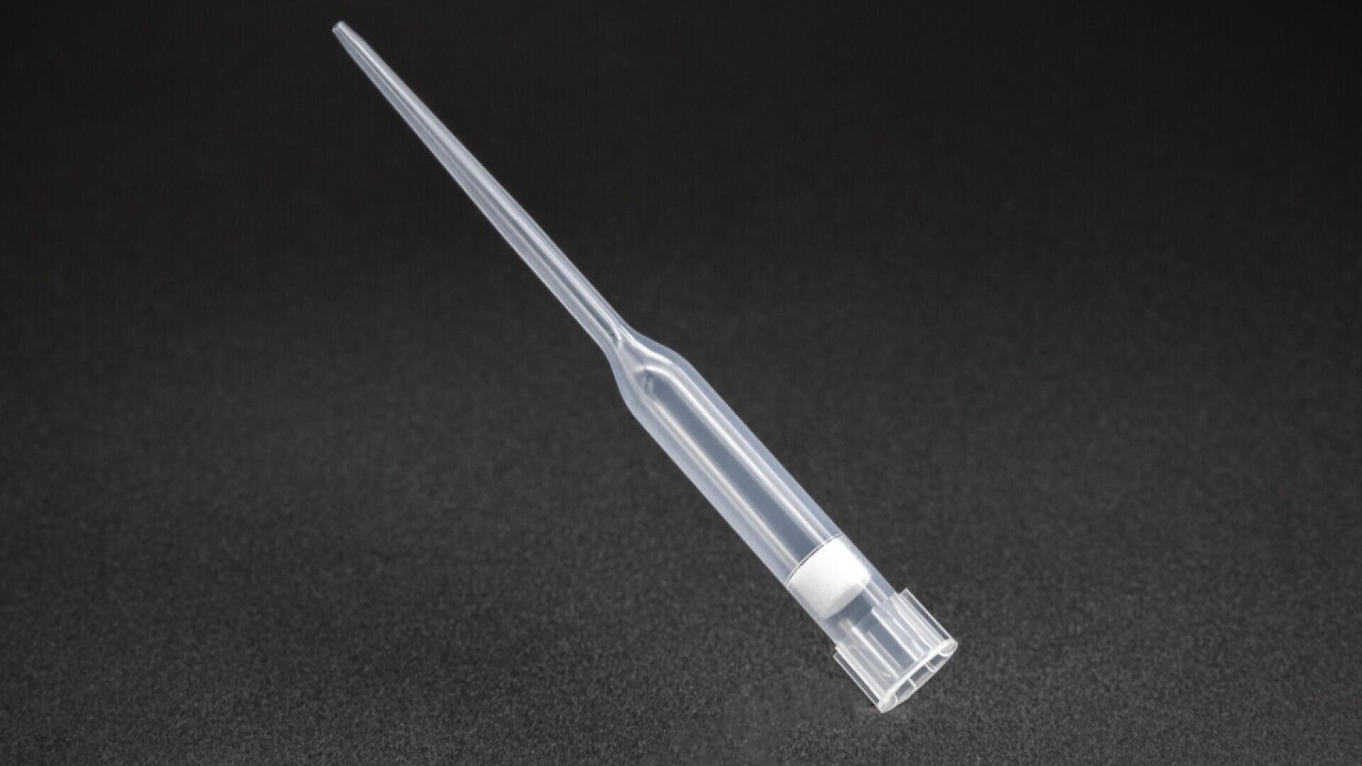 A transparent plastic pipette tip with a filter, lying diagonally on a black surface.