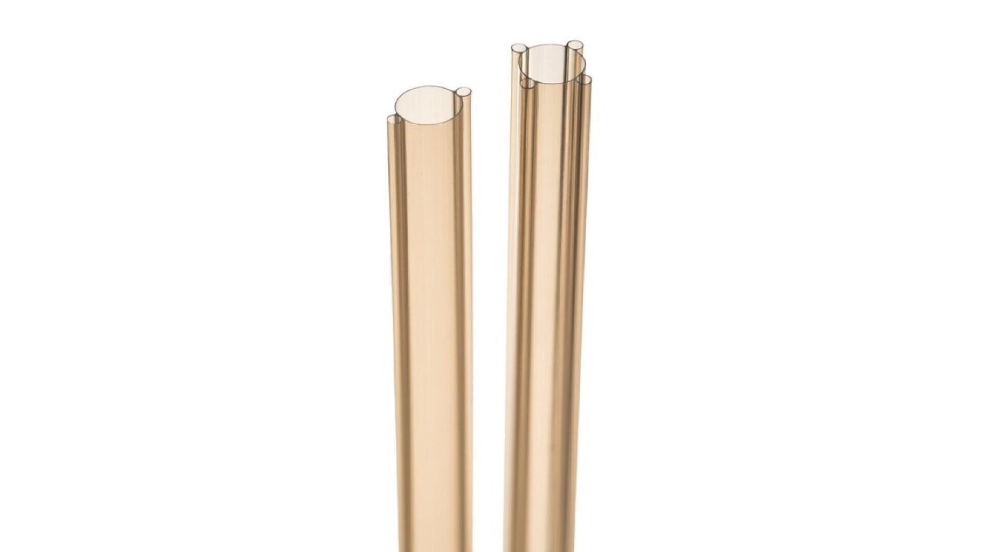 Two transparent light brown glass drinking straws are standing upright against a white background. The straws are cylindrical and smooth, with slightly rounded open ends.