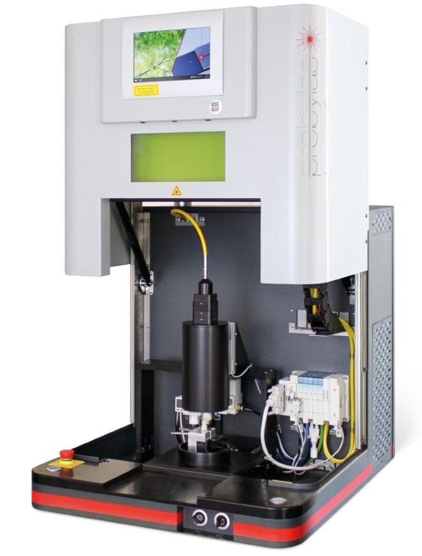 Ein Laborgerät mit digitaler Anzeige, offener Frontplatte, sichtbaren Drähten und Bauteilen, das für Präzisionsmessungen oder Materialprüfungen verwendet wird. Ein roter Not-Aus-Knopf befindet sich auf der linken Seite der Basis.