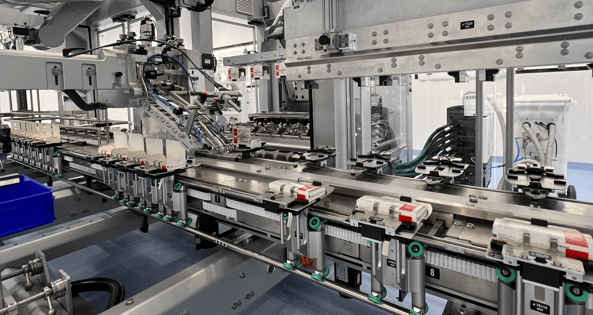 Nahaufnahme einer automatisierten Fertigungsstraße in einer Fabrik. Zu sehen sind Roboterarme und Maschinen, die kleine rechteckige Bauteile zusammensetzen und entlang eines Förderbandsystems bewegen.