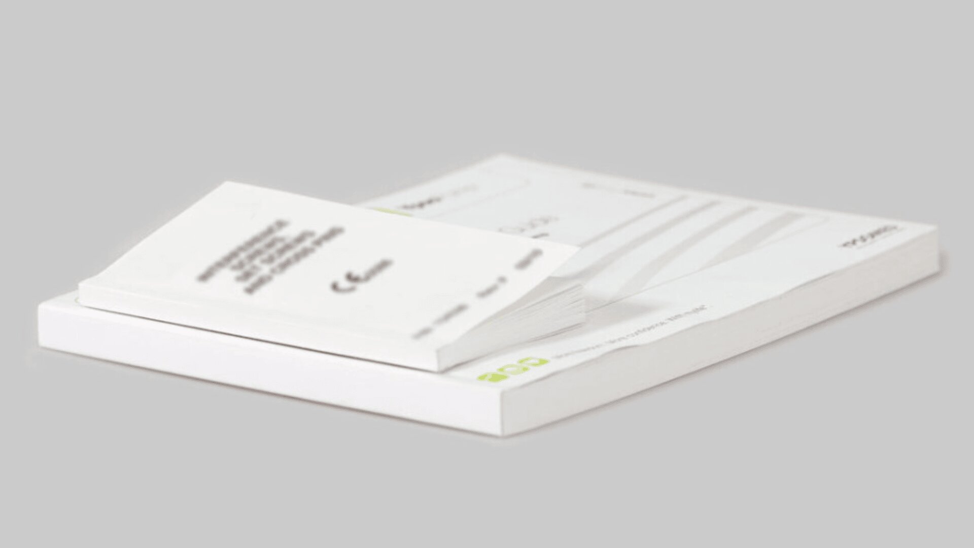 A stack of white business cards rests on top of a slightly larger stack of white paper sheets, all placed on a light gray surface. The cards have small, printed text visible.