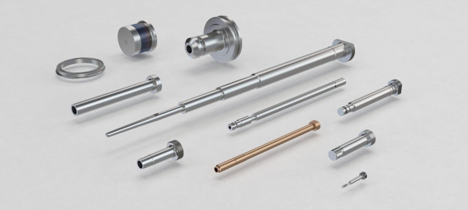 Eine Reihe von präzisionsgefertigten Metallteilen in verschiedenen Größen und Formen, einschließlich Stäben, Wellen und Ringen, die sauber auf einer hellgrauen Oberfläche angeordnet sind.