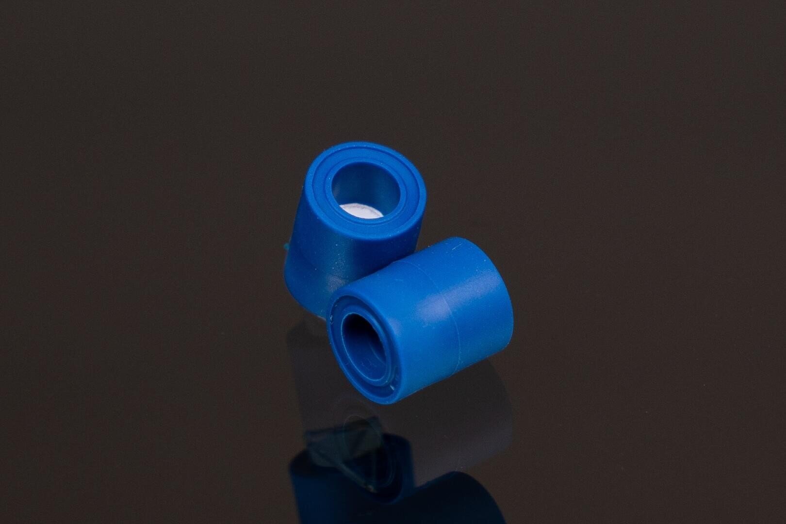 Zwei kleine blaue Plastikkappen, eine aufrecht und eine auf der Seite liegend, werden auf eine reflektierende dunkle Oberfläche gestellt.