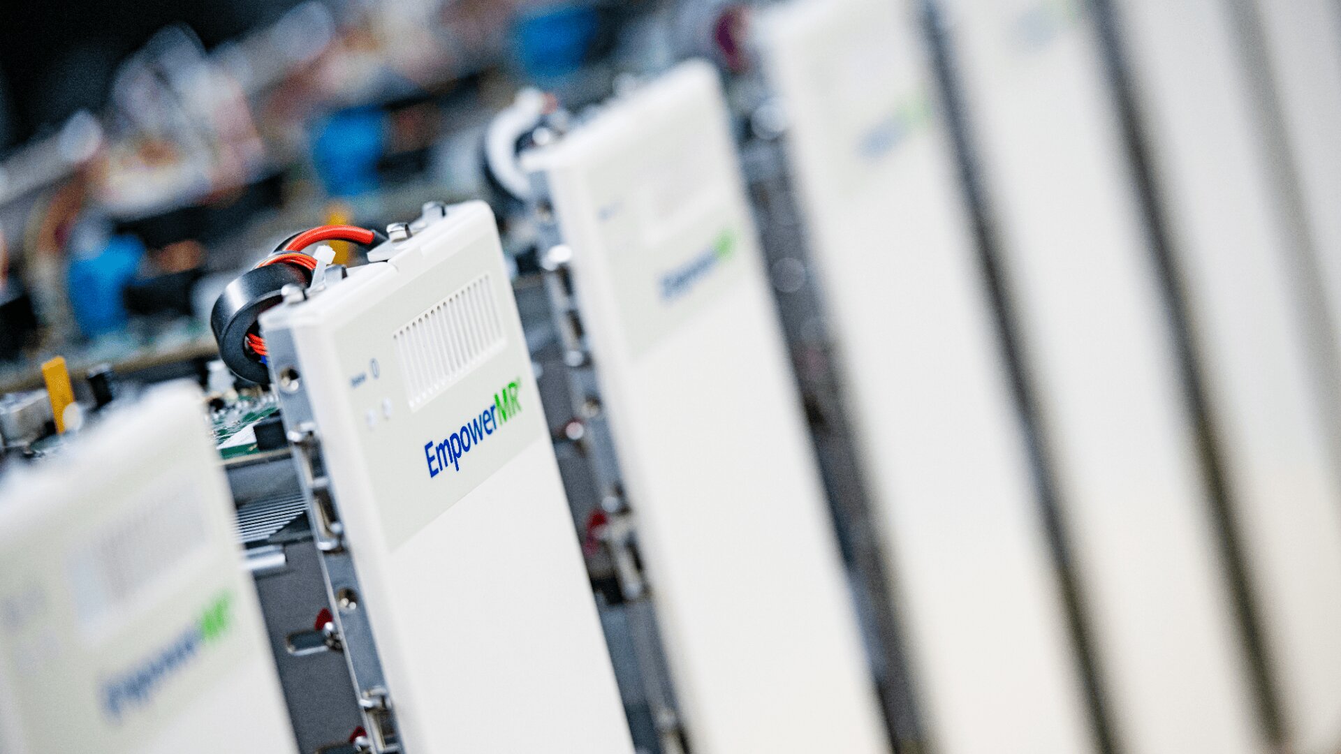 Nahaufnahme mehrerer weißer elektronischer Geräte mit der Bezeichnung „Empower RF“, die in einer Reihe angeordnet sind. Im Hintergrund sind Kabel und Schaltungskomponenten sichtbar.