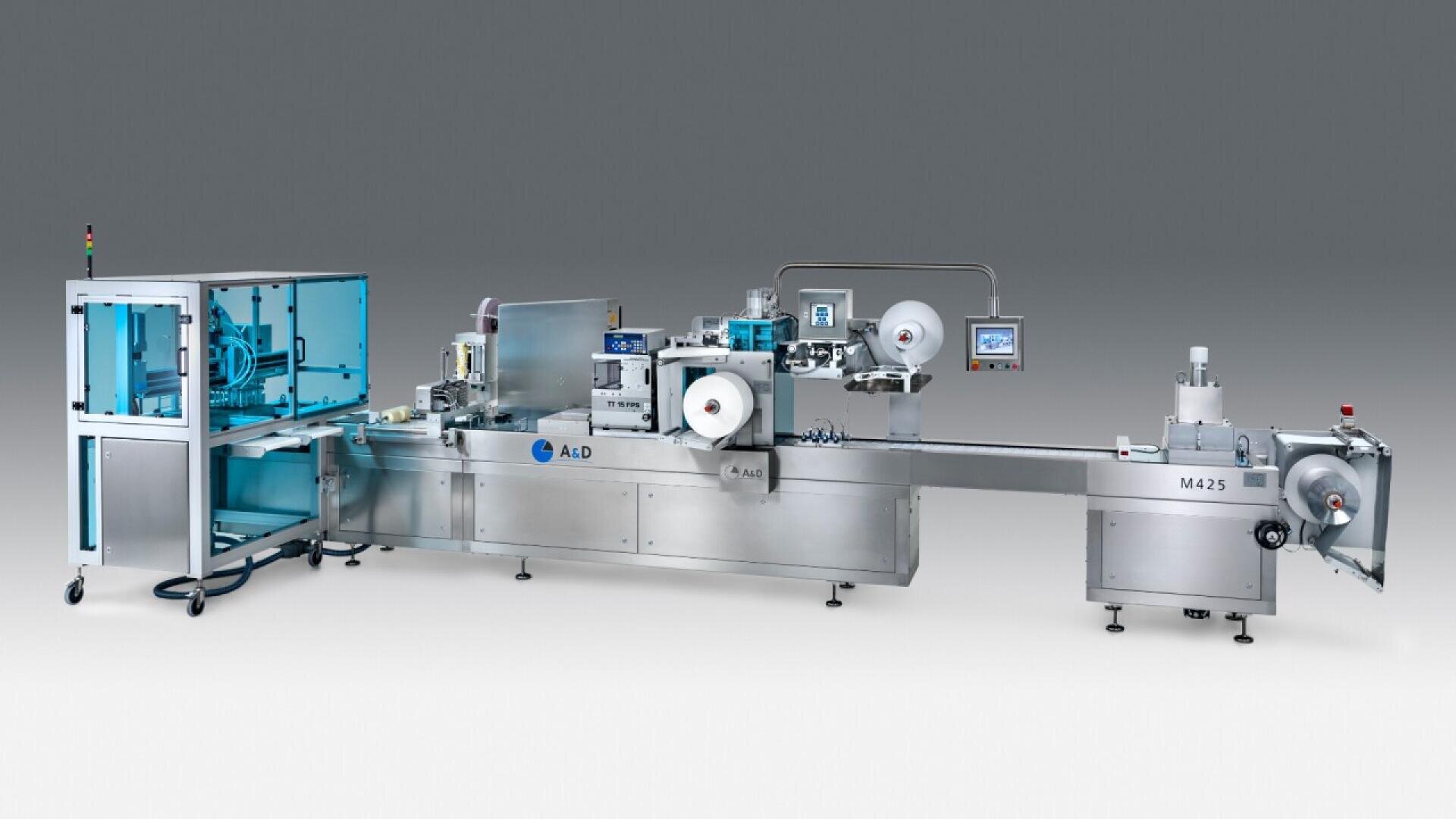 A large industrial packaging machine with metallic components, rollers, control panels, and a protective blue-tinted enclosure, set against a gradient gray background.