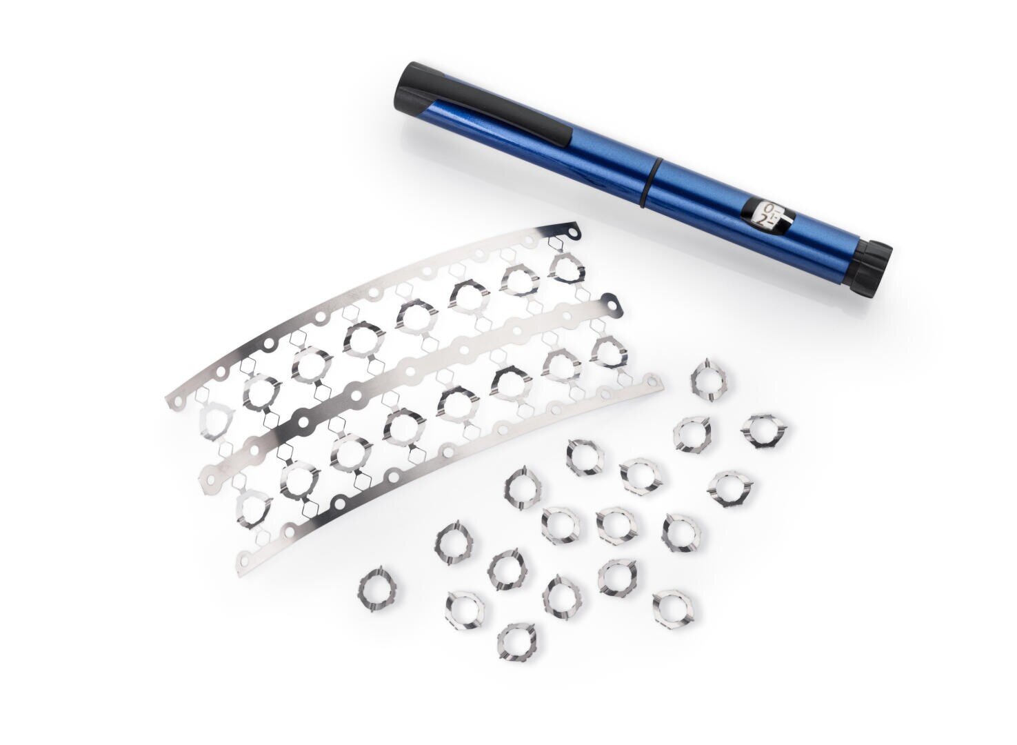 Ein blaues stiftförmiges Gerät, drei Metallstreifen mit kreisförmigen Ausschnitten und mehrere kleine sternförmige Metallringe, die auf einer weißen Fläche angeordnet sind.