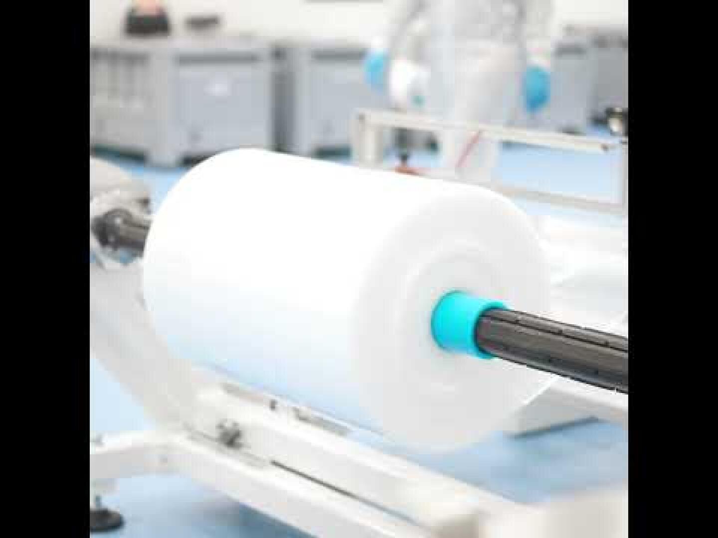 Eine große Rolle weißer Kunststofffolie auf einer Maschine in einer sauberen, industriellen Umgebung, mit einer Person in Handschuhen und Schutzkleidung im Hintergrund.