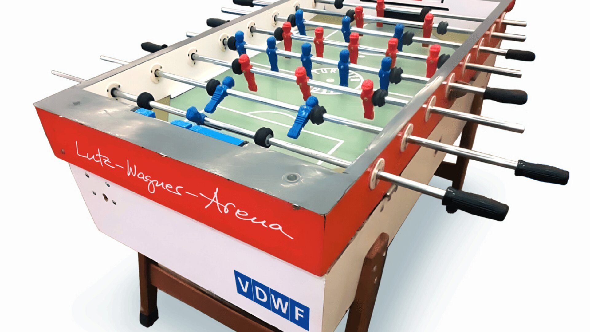 Ein rot-weißer Kickertisch mit der Aufschrift „Lutz-Wagner-Arena“ mit blau-roten Spielfiguren und schwarzen Griffen, stehend auf einem braunen Sockel mit seitlichem VDWF-Schild.