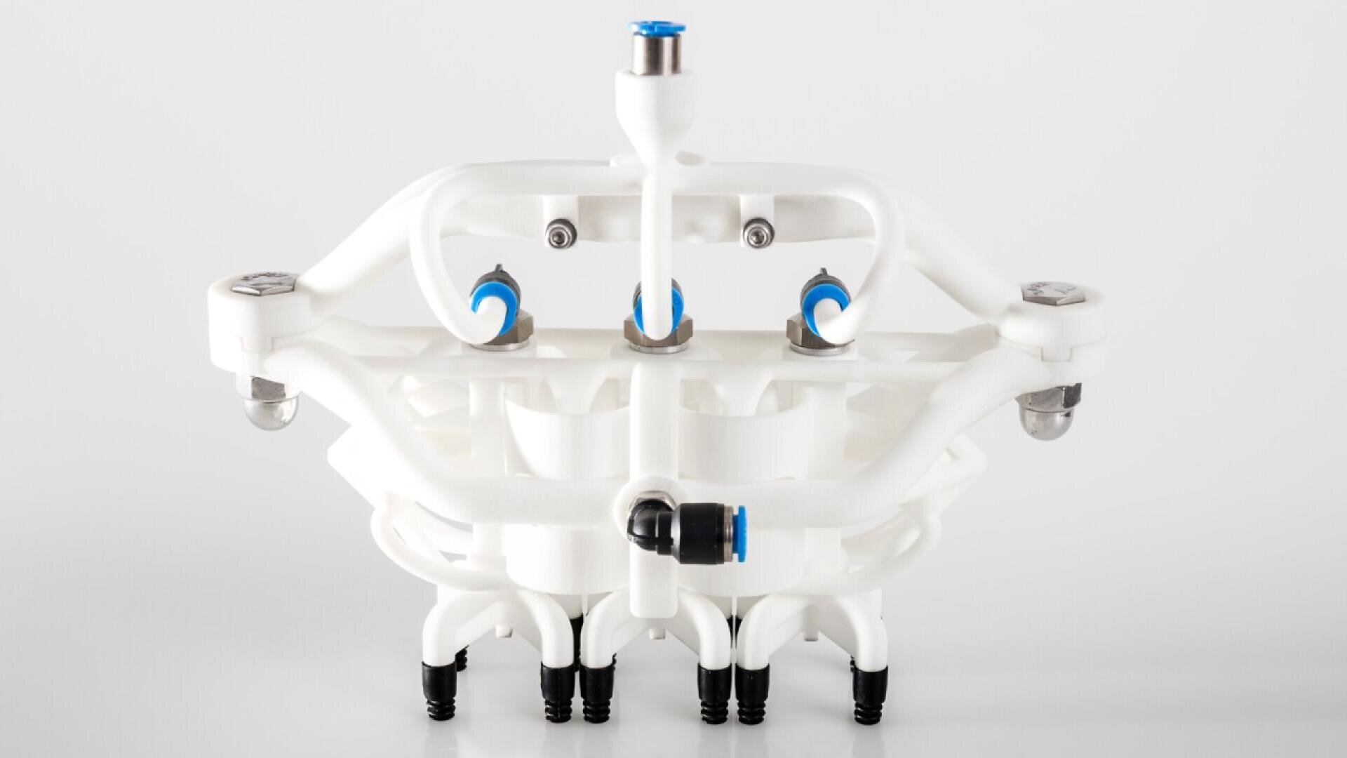 A white, multi-nozzle industrial component with blue and black connectors, featuring tubes and symmetrical design, set against a plain light background.