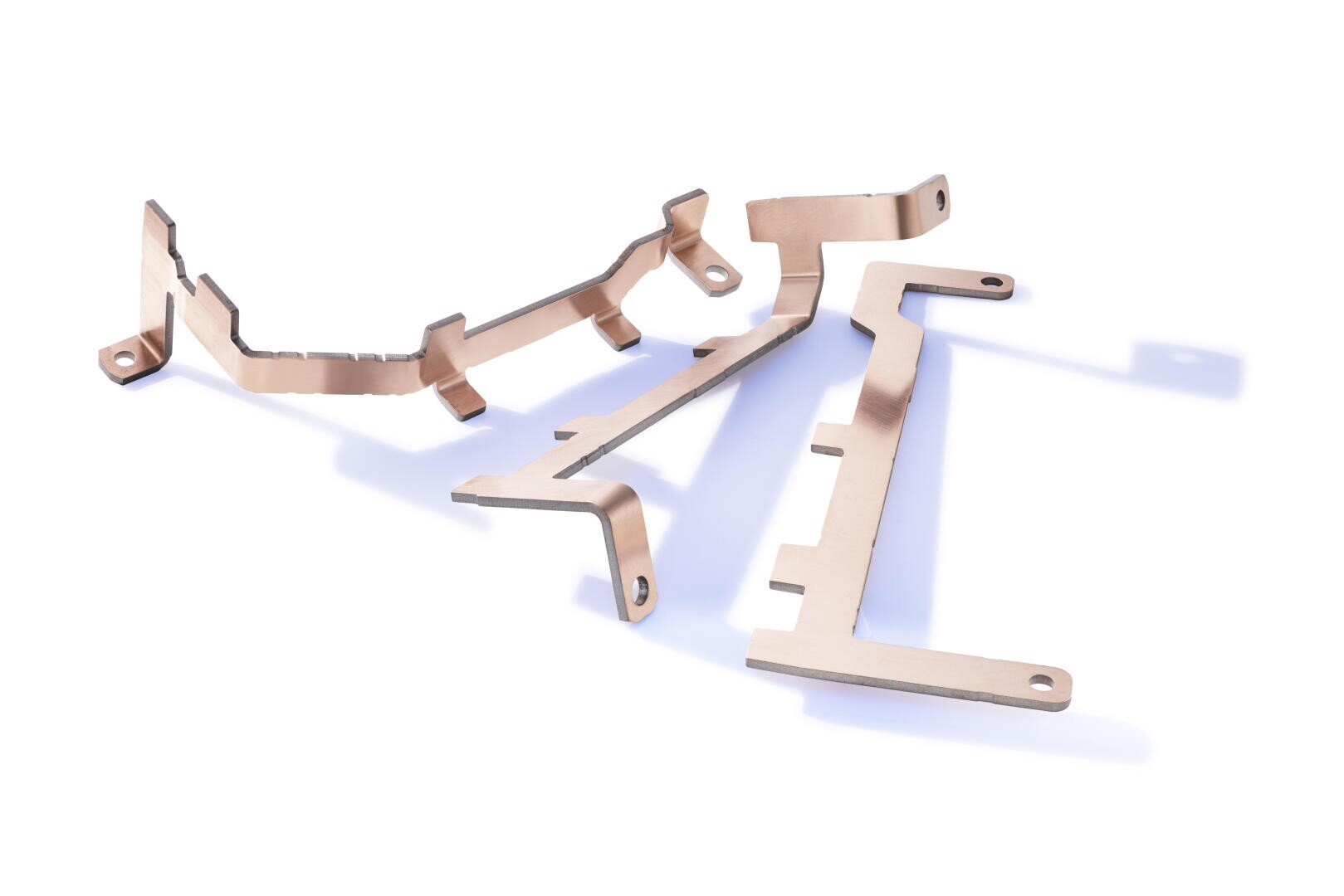 Zwei flache, unregelmäßig geformte Metallteile mit Ausschnitten und Befestigungslöchern, die auf einem weißen Hintergrund mit weichen Schatten angeordnet sind. Die Bauteile erscheinen kupferfarben und haben abgewinkelte Biegungen.