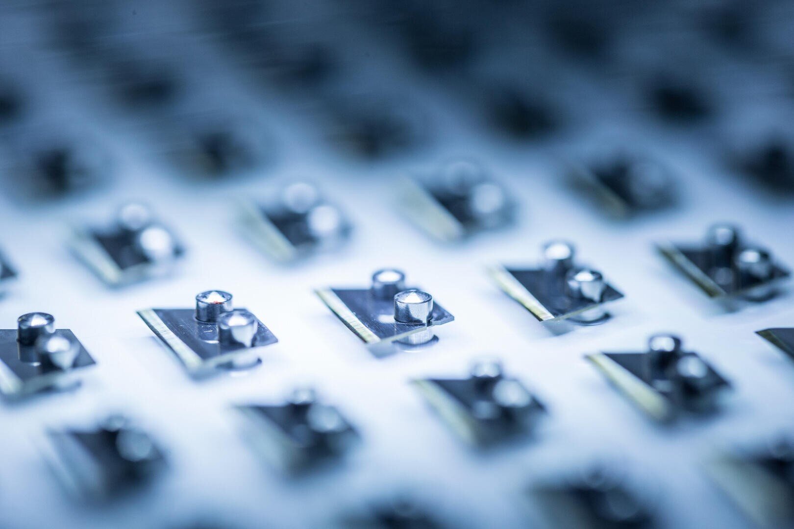 Nahaufnahme mehrerer kleiner metallischer elektronischer Komponenten, die auf einem Gitter montiert sind. Die geringe Tiefenschärfe erzeugt einen unscharfen Hintergrund und hebt die glänzenden Oberflächen hervor.