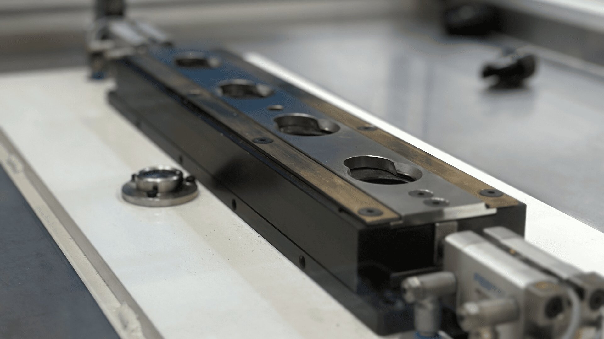 Nahaufnahme eines präzisen linearen Schienensystems aus Metall mit kreisförmigen Löchern und angebrachten Komponenten, montiert auf einer glatten Industrieoberfläche in einer Werkstatt oder Fertigungsumgebung.