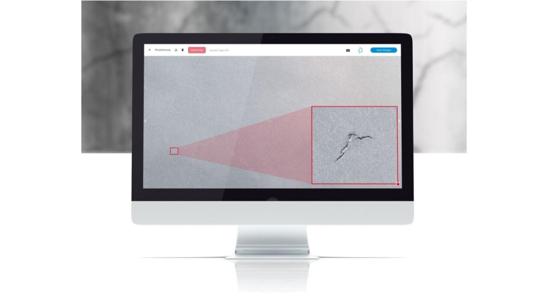 A computer monitor displays an image of a gray surface with a crack. A red box zooms in to show the crack in detail, highlighting it within a larger area of the surface.