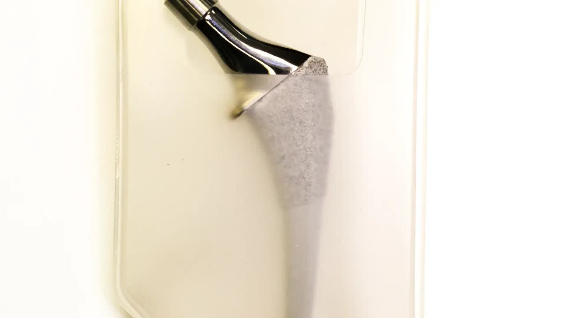 A metallic hip implant prosthesis with a polished upper section and a textured, tapered lower stem, placed on a light, neutral background.