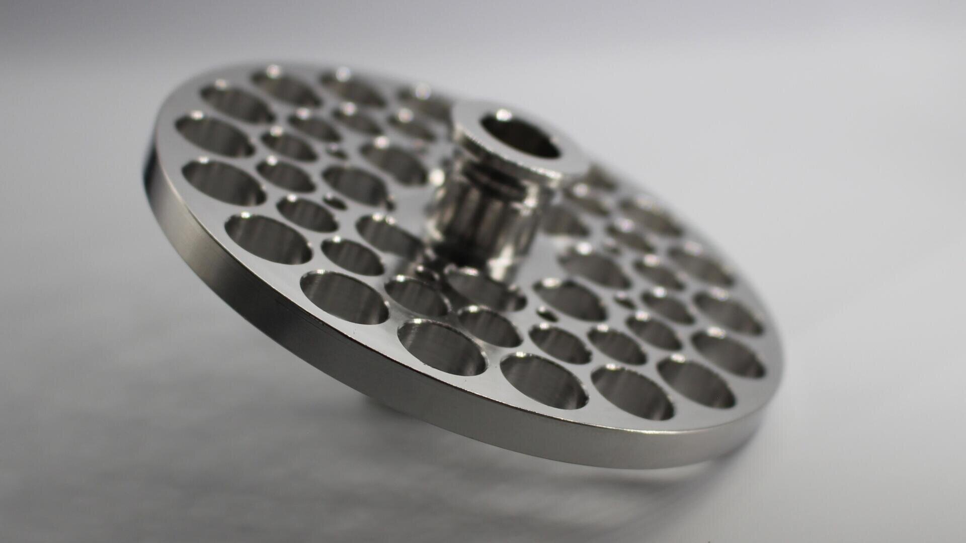 A metallic, circular component with multiple evenly spaced holes and a central hub, placed on a white background. The part has a polished, reflective surface and an industrial, machined appearance.