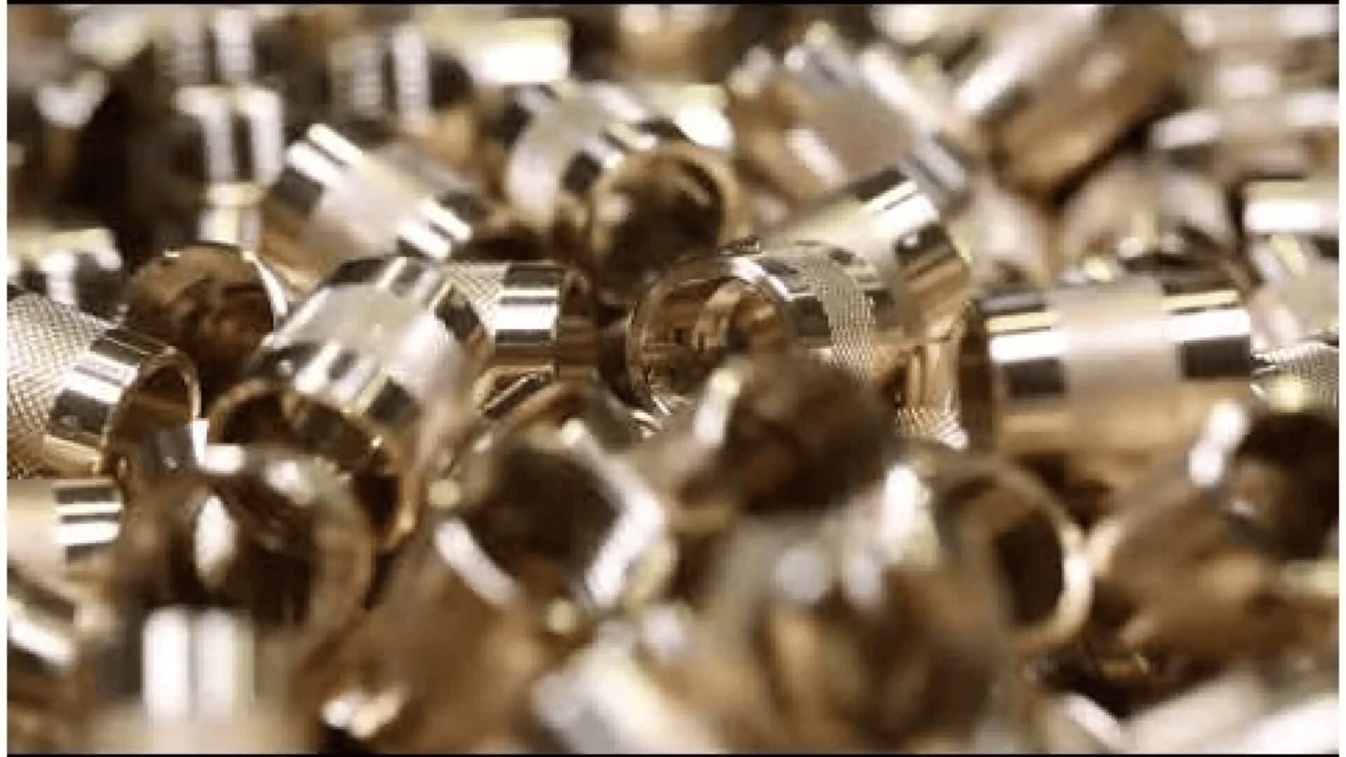 A close-up of a stack of shiny, cylindrical brass components or fittings stacked on top of each other in a random arrangement.