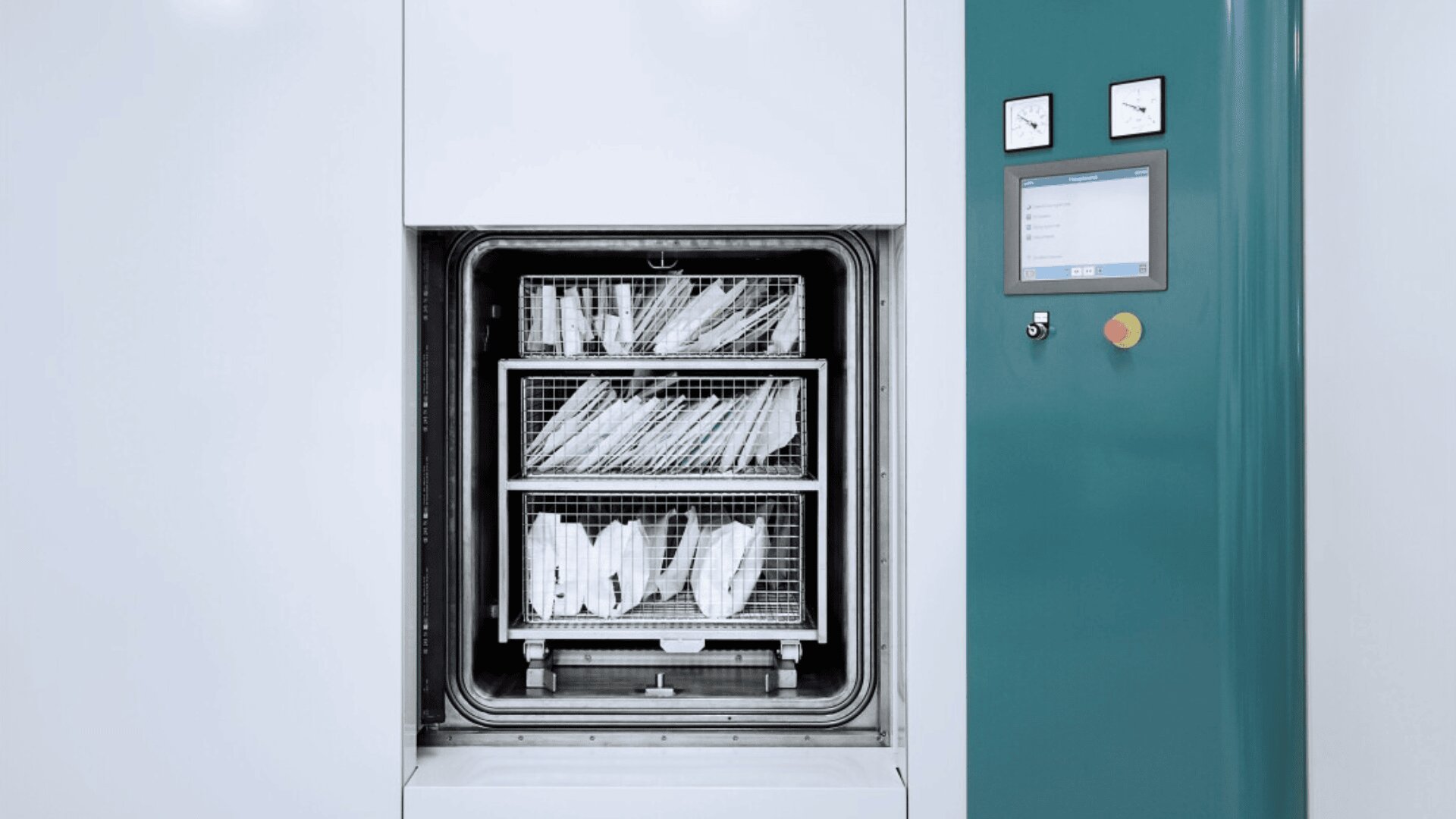 A medical sterilizer machine with its door open, showing trays filled with sterilized surgical instruments inside. The machine has a digital control panel and two analog gauges on the front.