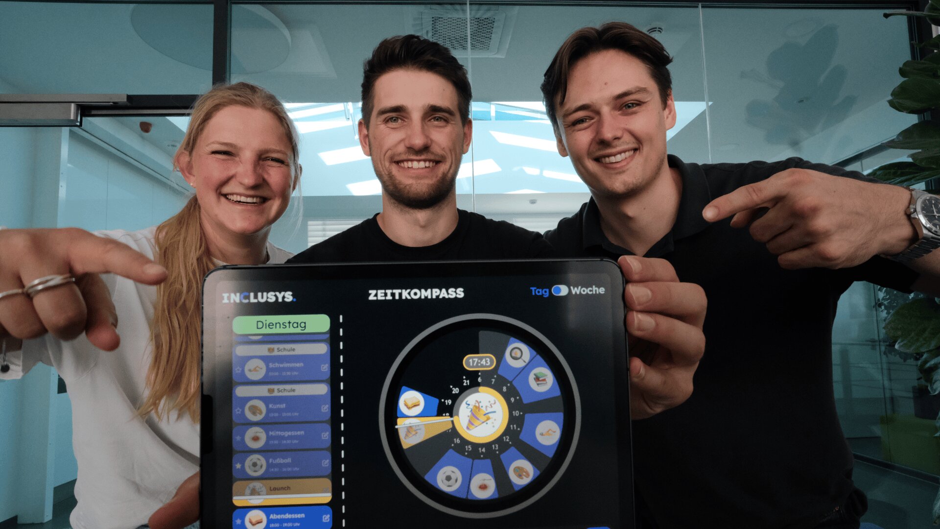 Drei lächelnde Menschen stehen hinter einem Tablet, auf dem die farbenfrohe Zeitmanagement-App „Zeitkompass“ läuft. Zwei von ihnen zeigen auf den Bildschirm und alle wirken in einer modernen Büroumgebung glücklich und enthusiastisch.