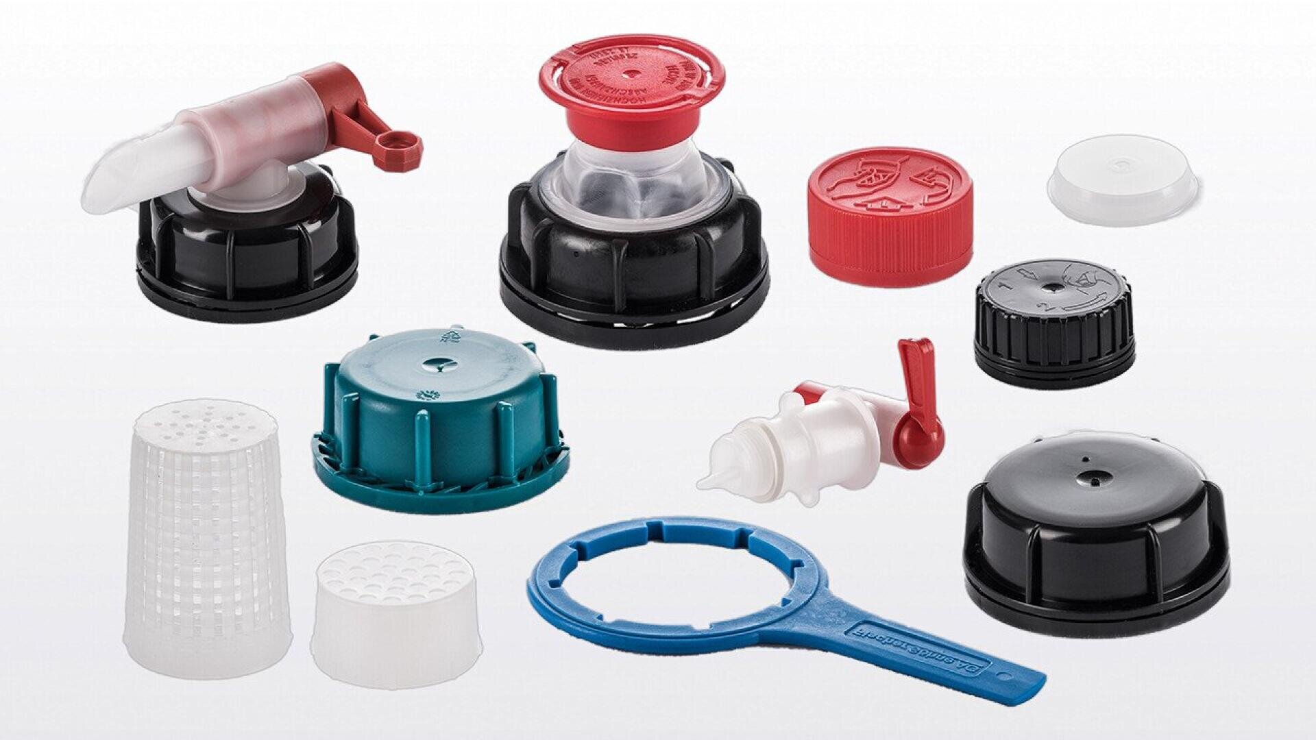 Assorted plastic caps, spouts, lids, and seals in various shapes, sizes, and colors, including black, red, teal, and white, arranged on a white background.