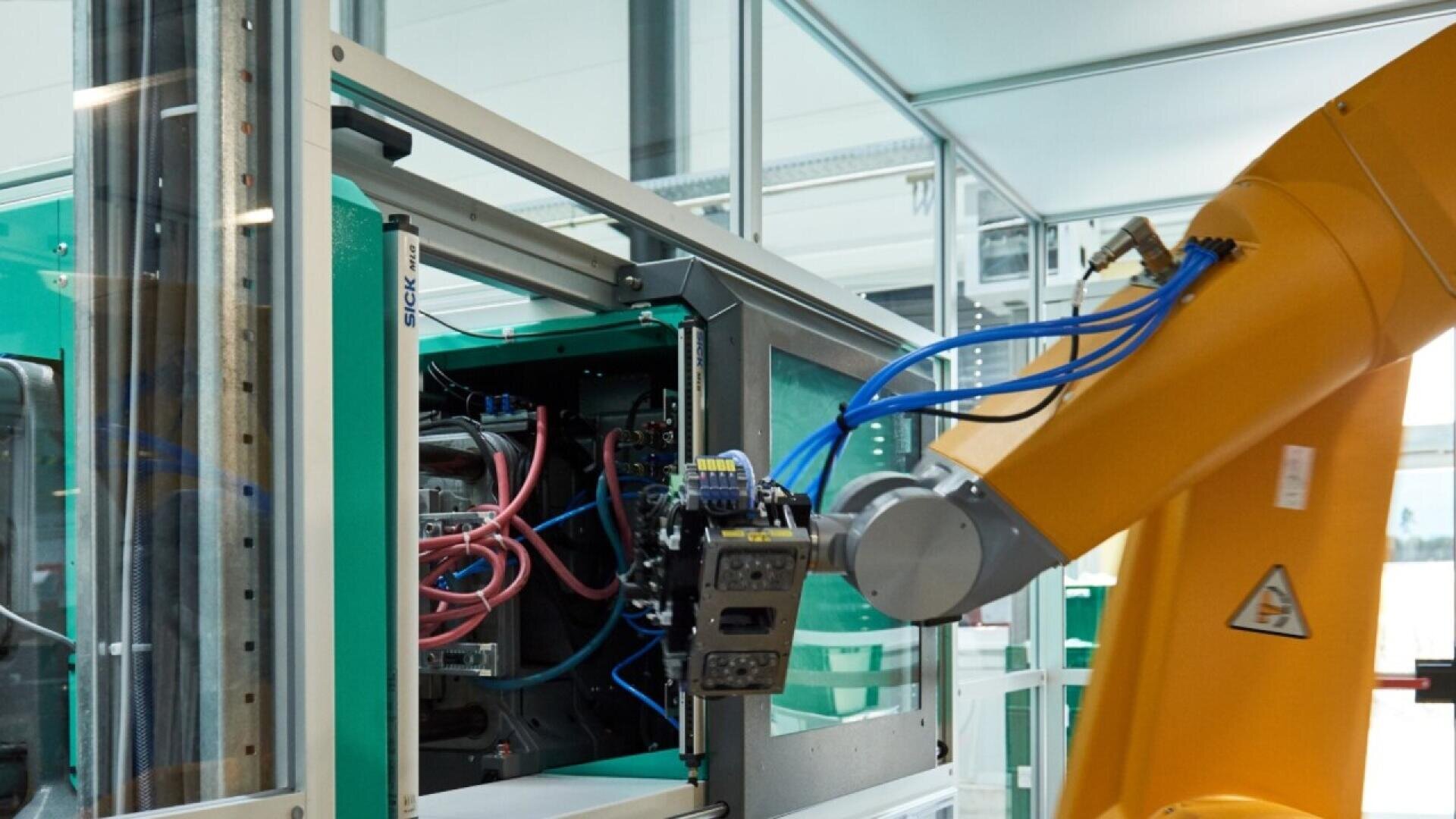 A yellow robotic arm operates machinery with exposed wires and components in a modern industrial facility, highlighting automation in a manufacturing environment.