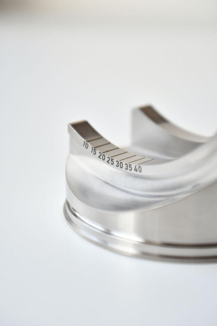 Close-up of a bent metal object with engraved measurement markings in increments of five from 10 to 40 on a smooth, reflective surface with a white background.
