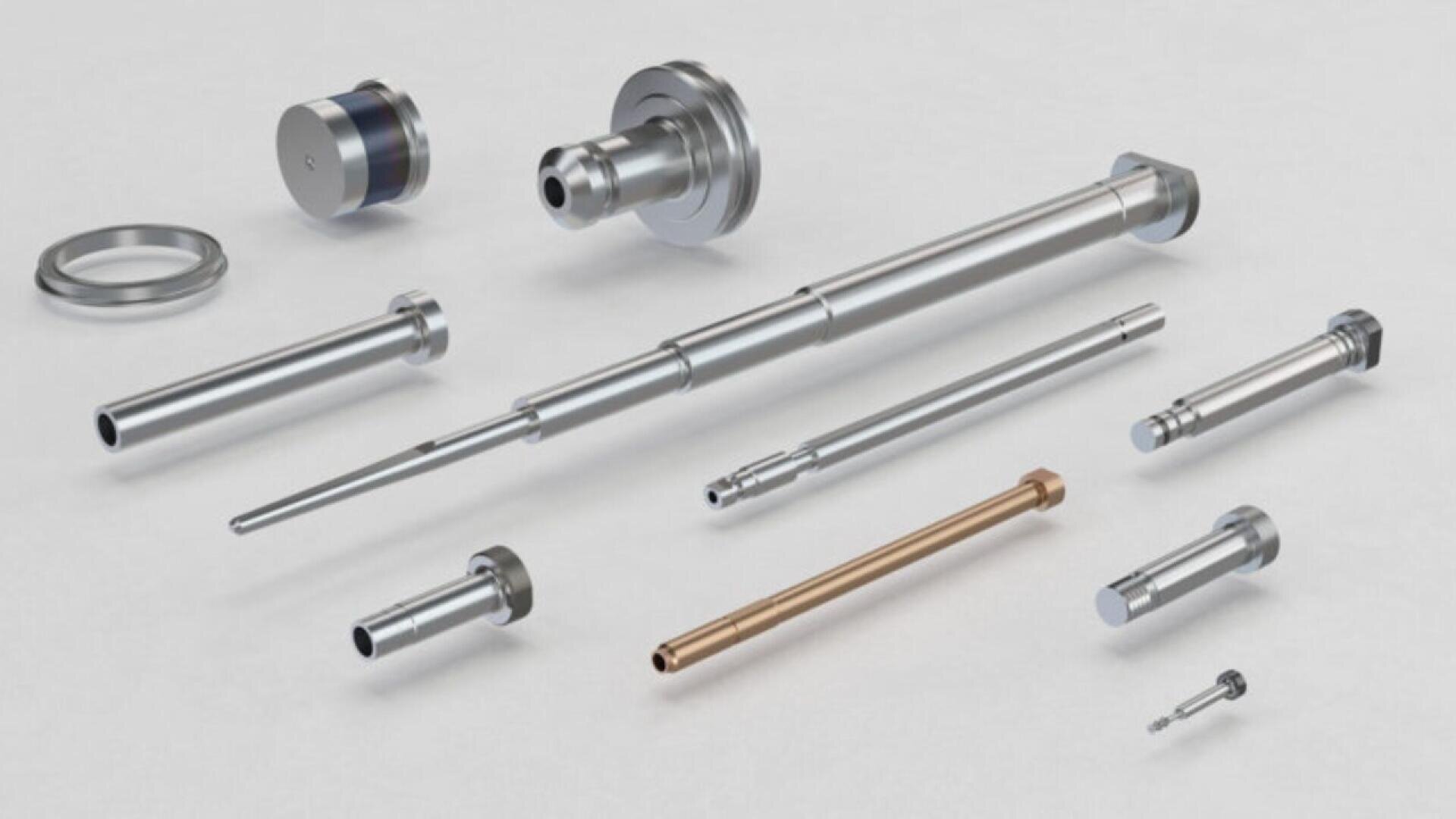 A variety of precision metal components and shafts of different sizes and shapes are neatly arranged on a light surface, displaying intricate machining and polished finishes.