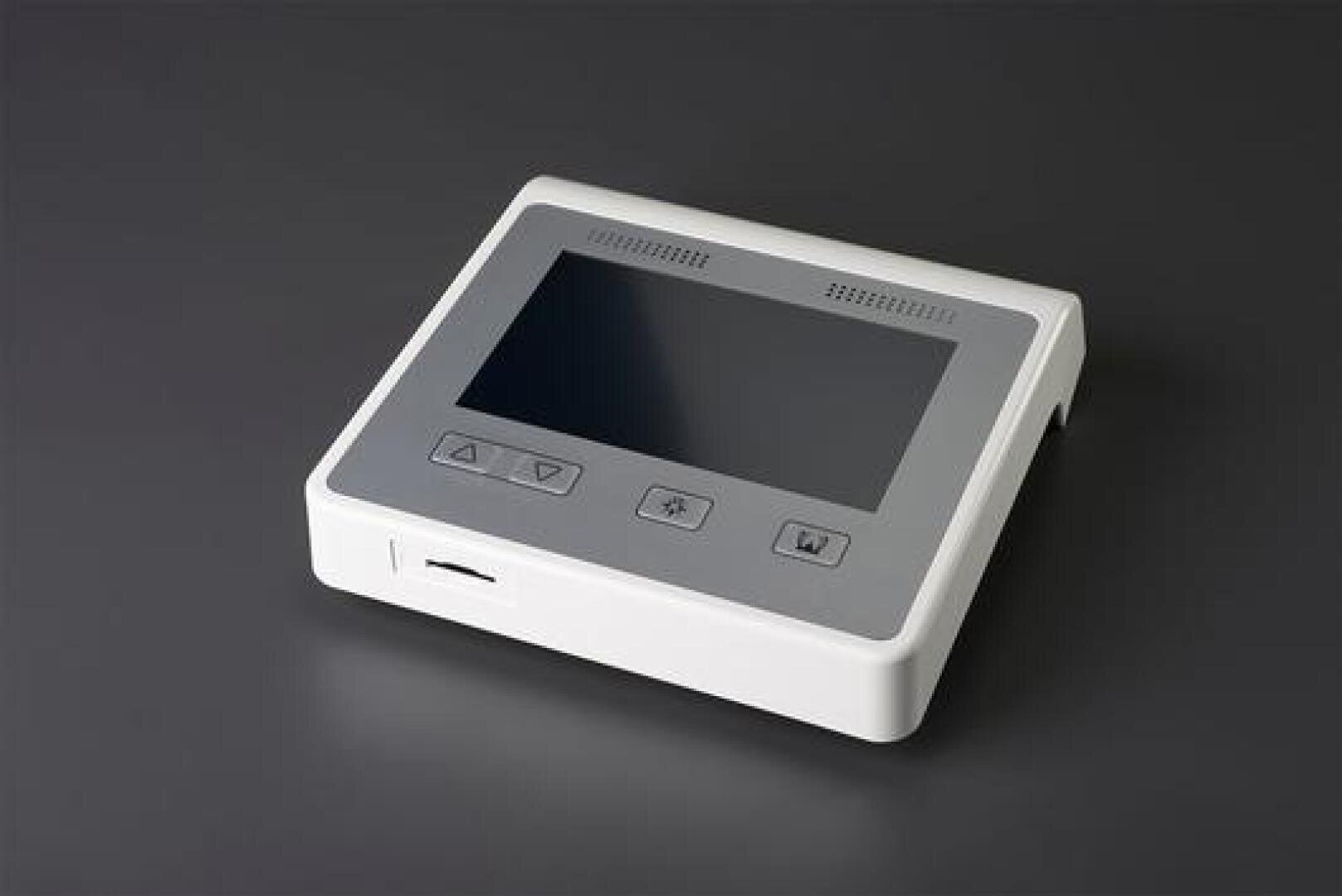 A white electronic device with a large black screen and three buttons below it, standing on a dark grey surface. The device also has a slot on the left side.