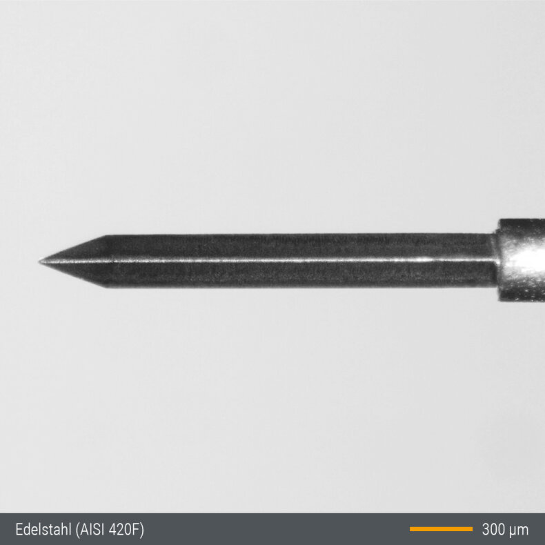 Close-up image of a pointed metallic needle with a cylindrical shaft, photographed against a plain background. A scale bar at the bottom right indicates 300 micrometers. Text reads Edelstahl (AISI 420F) at the bottom left.
