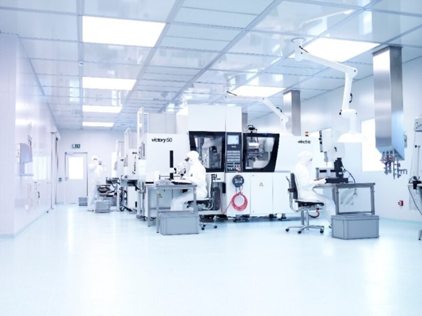 Ein helles, sauberes Labor mit Wissenschaftlern in Ganzkörper-Schutzanzügen, die an hochmodernen Maschinen und Computern arbeiten; der Raum hat weiße Wände, eine gekachelte Decke und eine makellose, hochtechnologische Atmosphäre.